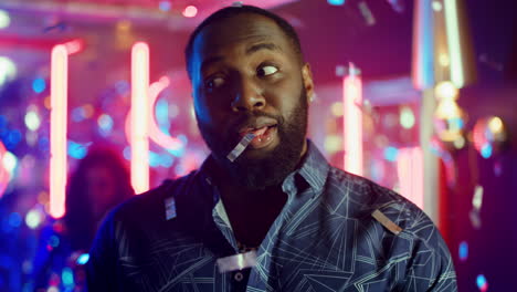 african american man trying to spit foil at party. guy posing under confetti