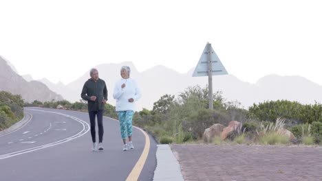 happy senior biracial couple running on road in mountains