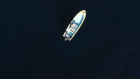 birddseye view of fishermen moving around boat in deep blue water