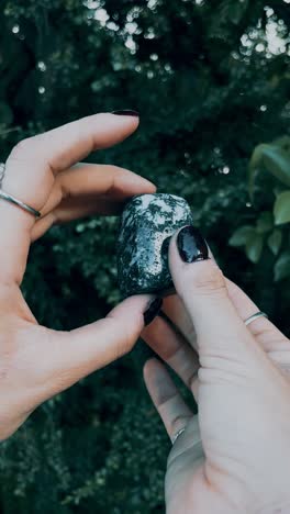 hands holding a dark green and white gemstone
