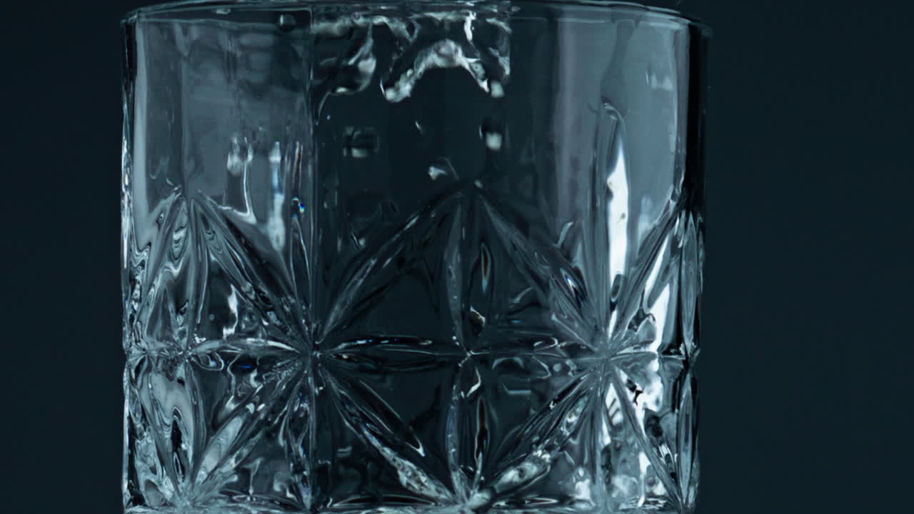 un primer plano de un vaso lleno de agua en un fondo oscuro. gotas transparentes cayendo.