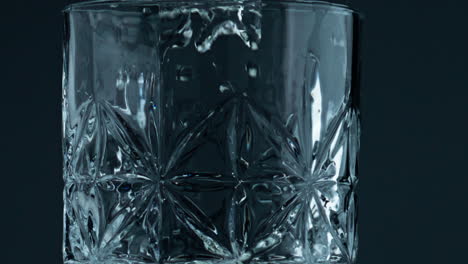 un primer plano de un vaso lleno de agua en un fondo oscuro. gotas transparentes cayendo.