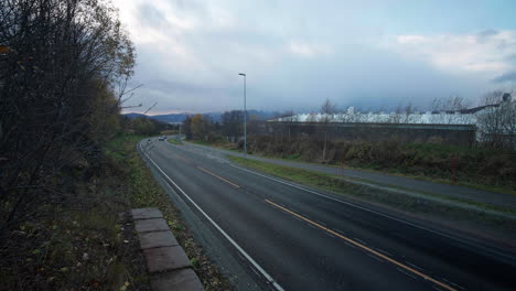 Fast-traffic-on-road-in-Norway,-cars-passing-by-in-high-speed-and-clouds-floating-on-the-sky