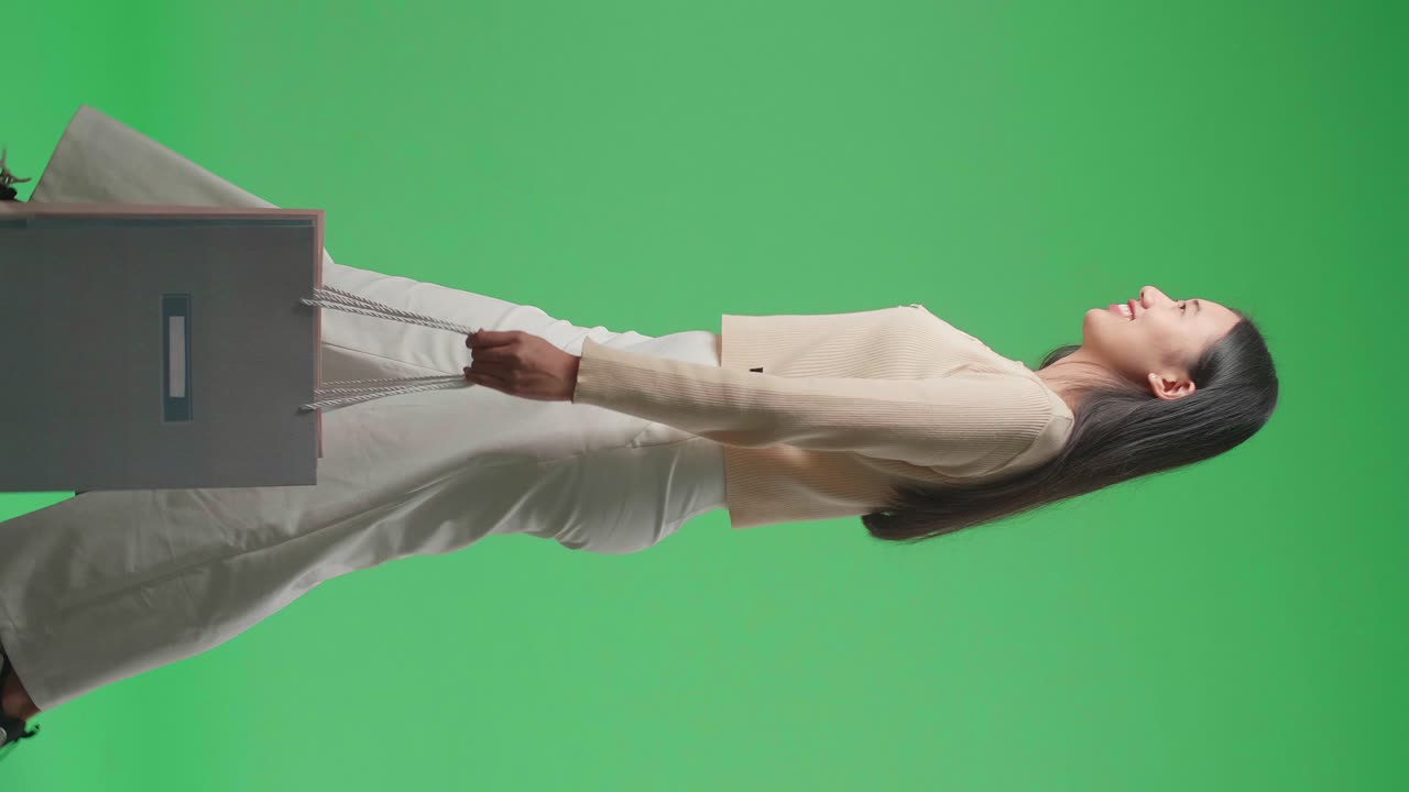 Side View Of An Asian Shopping Woman With Shopping Bags Smile And Walking In Front Of Green Screen