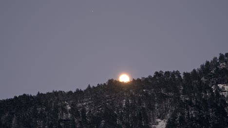 beautiful bright shining full moon rising behind trees and over snow covered mountain