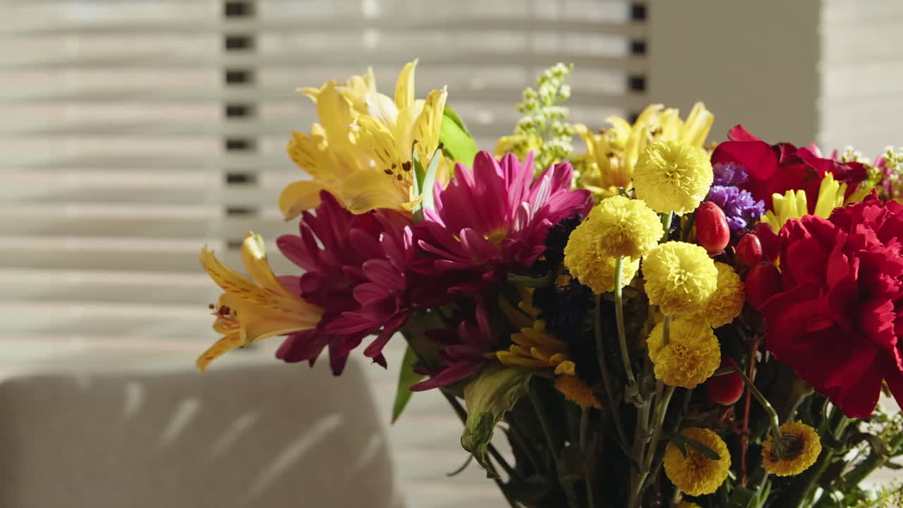 Bright, colorful bouquet of flowers on a table with soft sunlight shining through blinds
