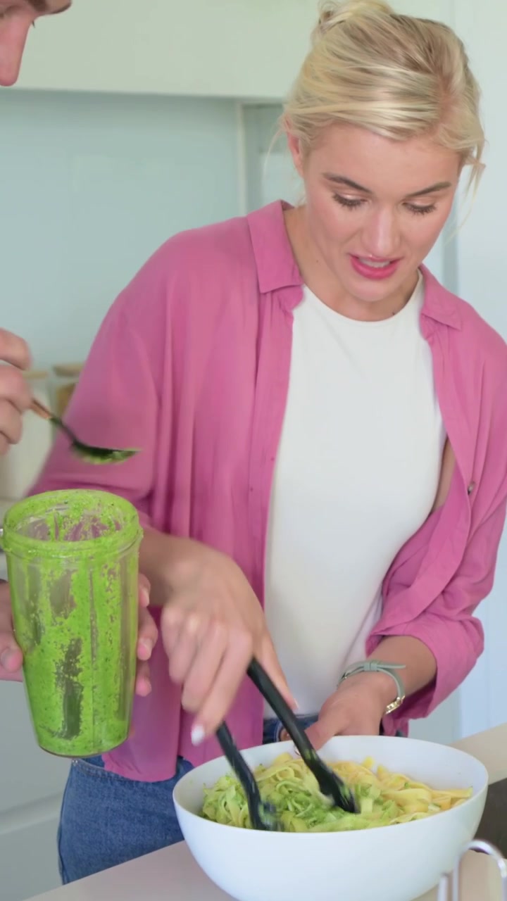 Video verticale: Un uomo in denim solleva il boccale del frullatore e condisce gli zoodles in cucina, mentre una donna usa le pinze.