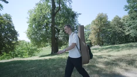 young man walking with guitar on street near forest