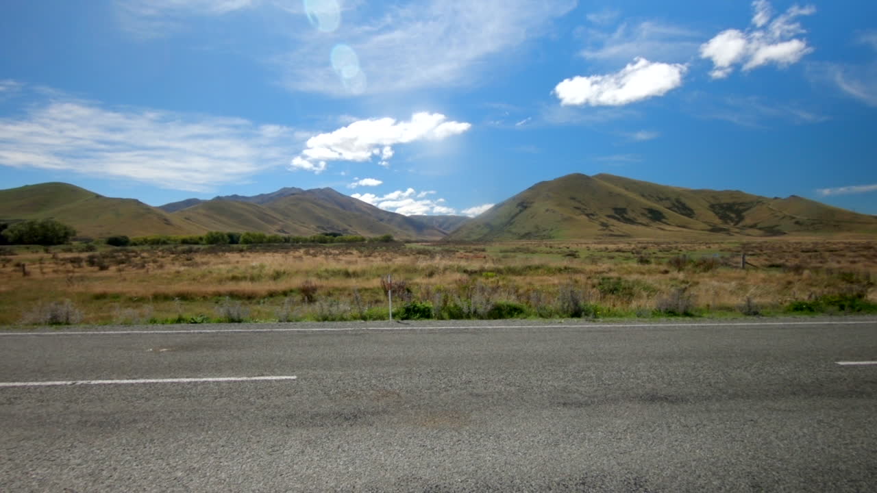 Un'auto attraversa la scena in primo piano con un incredibile paesaggio montano neozelandese sullo sfondo in una splendida giornata di sole