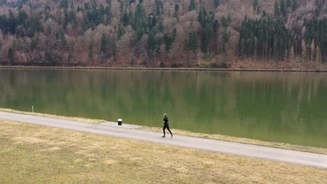 Beim-Schwenken-Fliegt-Die-Drohne,-Die-Dieses-Filmmaterial-Gefilmt-Hat,-Neben-Einem-Weg,-Auf-Dem-Ein-Jogger-In-Einem-Schwarzen-Anzug-Läuft