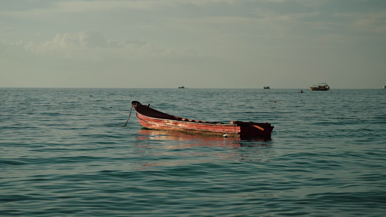 A red wooden fishing boat rests calmly on the turquoise waters off Ko Tao island, Thailand
