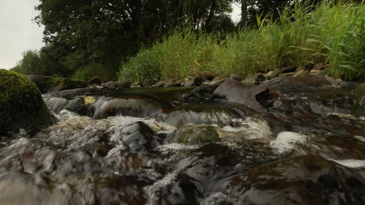Low angle close-up shot of a small stream flowing over rocks creating a waterfall