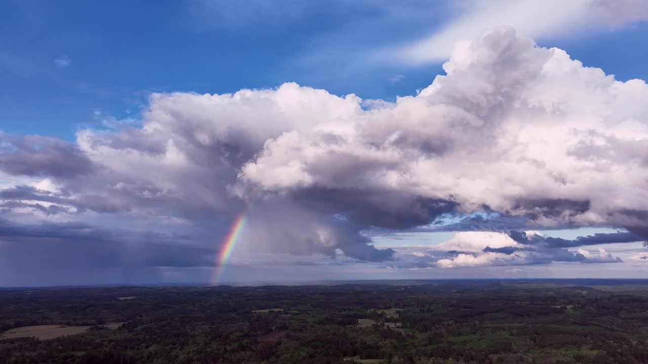 Dunkle Gewitterwolken ziehen über eine weite Waldlandschaft mit einem deutlichen Regenbogen. Drohnenaufnahmen fangen die atmosphärische Spannung und die Wetterbedingungen ein, die typisch für ein französisches Sommergewitter sind.