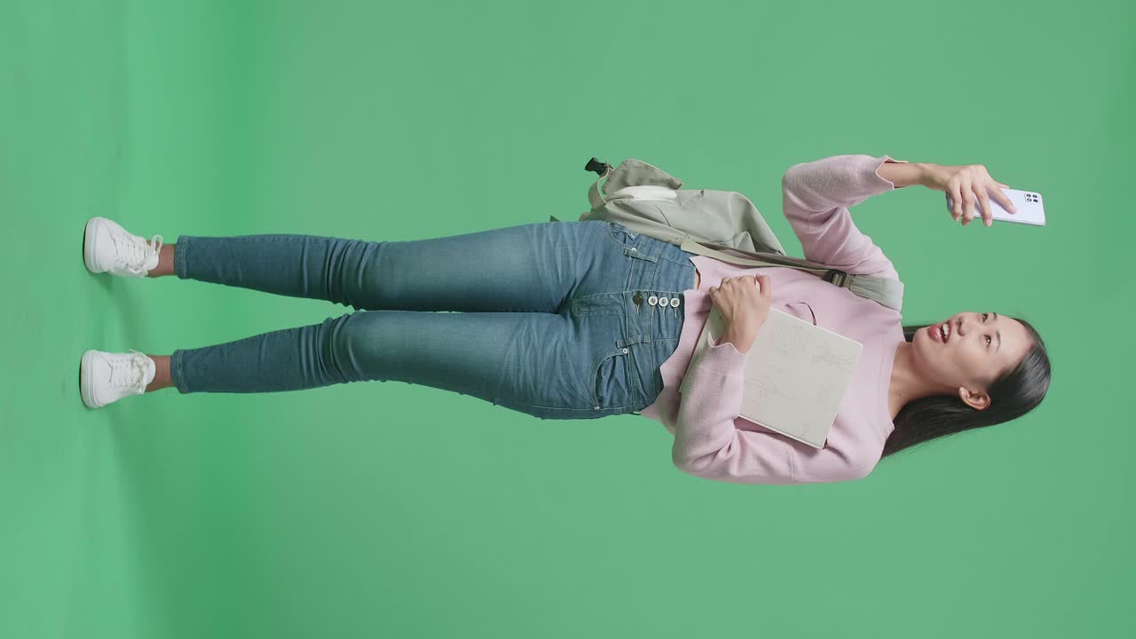 녹색 스크린 스튜디오에서 휴대전화로 비디오 통화를 하는 아시아 여성 학생의 몸이 가득 차 있습니다.