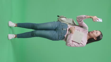 cuerpo lleno de estudiante asiática haciendo una llamada de video por teléfono móvil en el estudio de pantalla verde