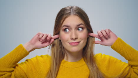 Portrait-of-smiling-woman-covers-her-ears-with-fingers-at-camera-in-studio.