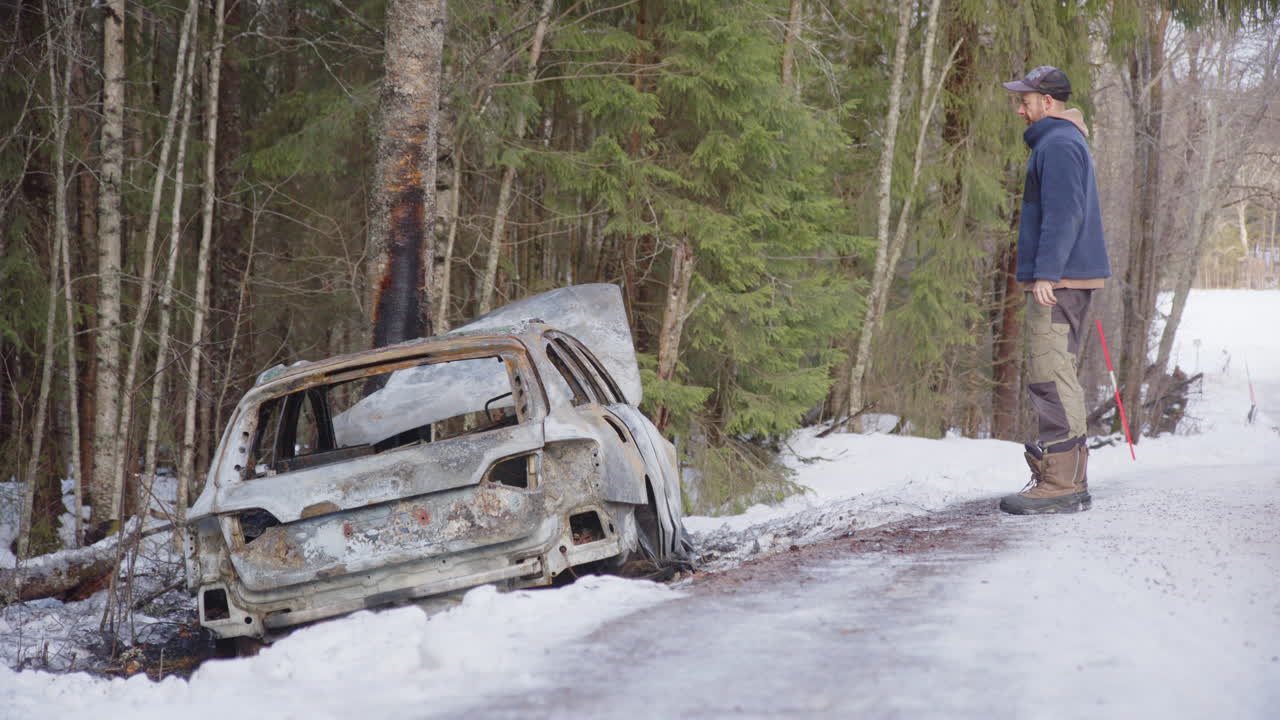 Dejected male owner of wrecked car that crashed off icy road into tree