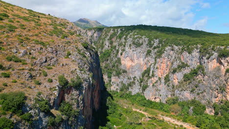 Aerial-drone-tilt-up-shot-of-dry-riverbed-along-mountain-slope-beside-Gjipe-beach-in-Albania-on-a-sunny-day