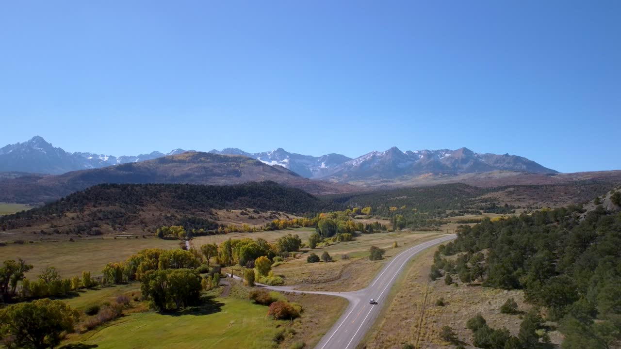 drone volando hacia atrás sobre una carretera de montaña en colorado mientras los coches conducen hacia adelante hacia las montañas rocosas en un día sin nubes durante el otoño