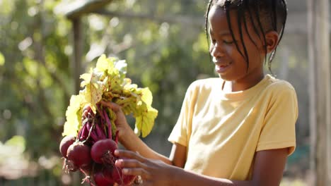 portrait of happy african american boy holding vegetables in sunny garden, slow motion