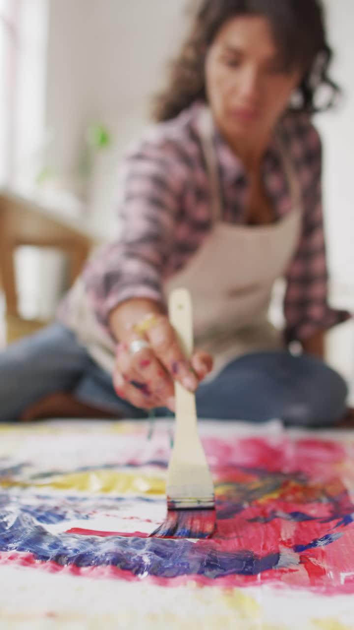 Vertical video of biracial female artist painting on floor in studio