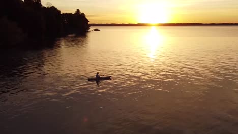 aerial shot of man paddling across a lake at sunset