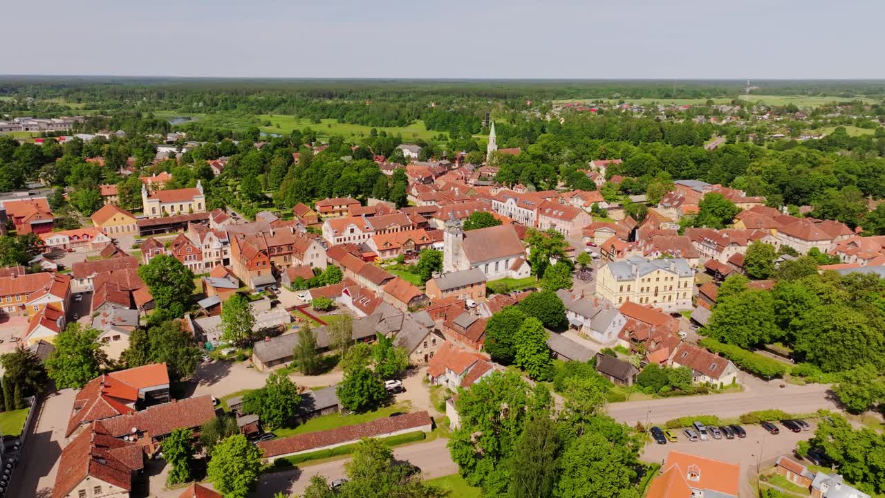 Drone glides over Kuldīga old town rooftops, summer light, dynamic lateral view