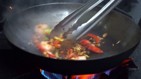 professional chef adding xo sauce into stir fry seafood dish, spicy prawns with garlics and capsicums cooking in hot pan, delicious aromatic smokes in commercial kitchen setting