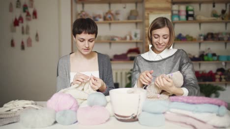 Two-woman-knitter-talking-and-smiling-at-work-table-in-studio