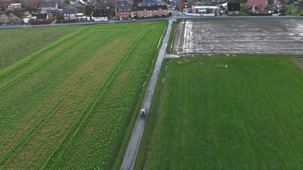 Tractor on path on agricultural farm fields in winter. Rainy day in american suburb. Top down shot. Aerial tracking shot.