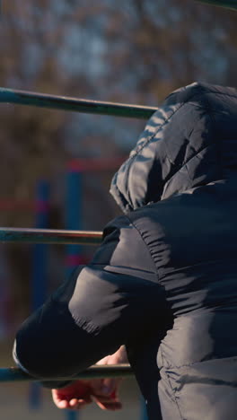 primer plano de dos personas descansando sus manos en una barra de hierro, ambos con una chaqueta con capucha y el otro en el fondo borroso, con un edificio borroso en la distancia