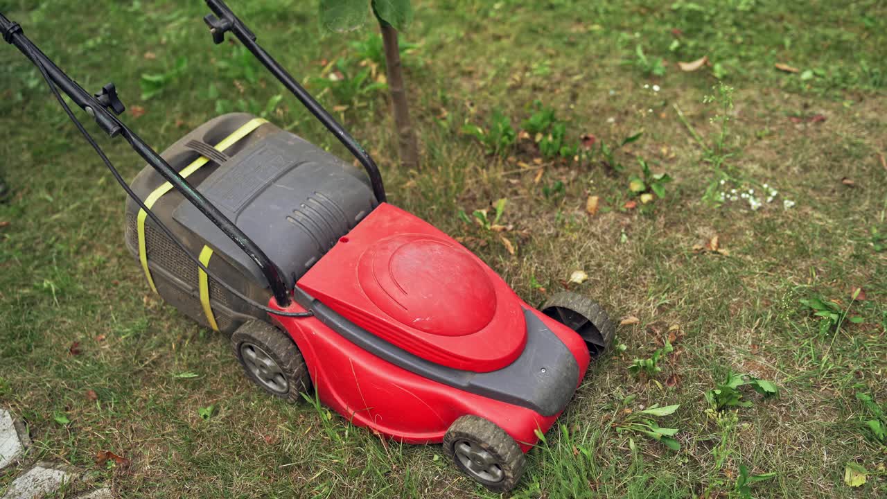 A lawn mower is cutting green grass. Young boy with a lawn mower is working in the backyard