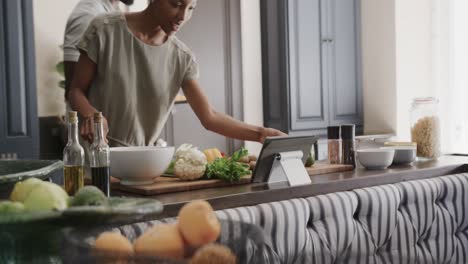 feliz pareja afroamericana cocinando y usando tableta en la cocina en cámara lenta