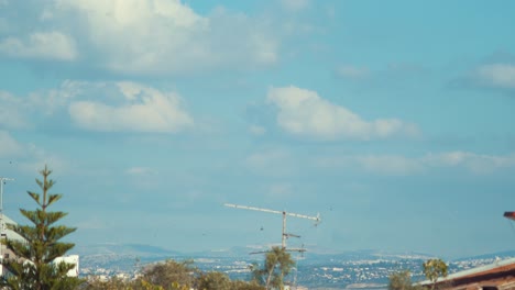 Time-lapse-shot-of-a-surfing-clouds-in-the-blue-skies,-green-tree,-hill-in-the-background,-4K-Video