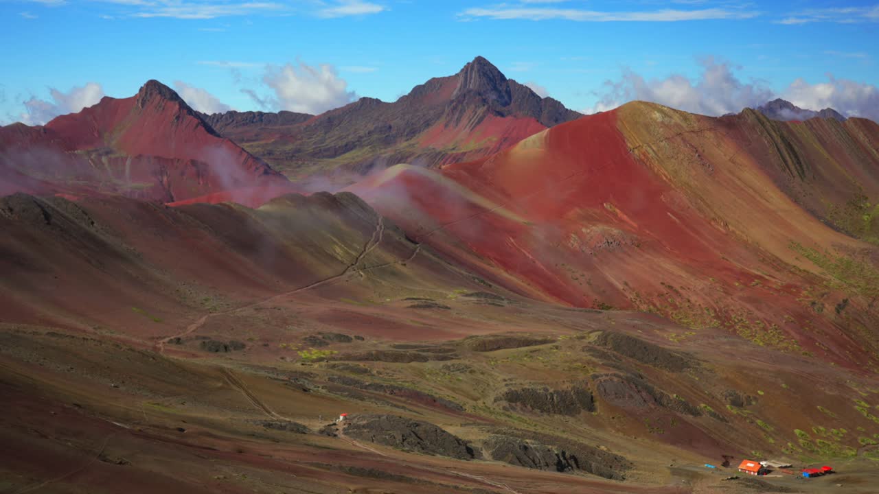 Paesaggio naturale del Perù: la Montagna Arcobaleno (Vinicunca) e la Valle Rossa nelle Ande peruviane, catena del Vilcanota. Un sentiero nella nebbia, una collina a sette strati colorati e striati. Mattina soleggiata con cielo blu e nuvole. Vista panoramica con zoom.