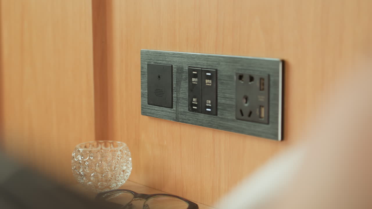 Visitor plugs in their charger at hotel. Guest quickly attaches their device charger beside lamp. Traveler promptly connects their electronic device to hotel power socket for charging