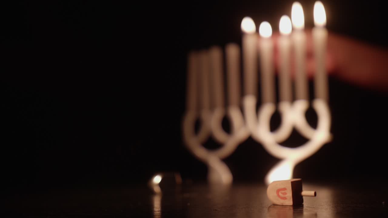 Hand zündet Chanukka-Menora-Kerzen an, mit Dreidel und Gelt.
