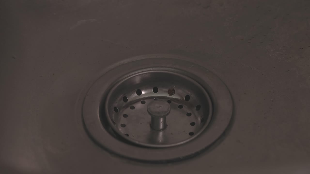 Close-up shot of water flowing down a kitchen sink as hands wash dishes