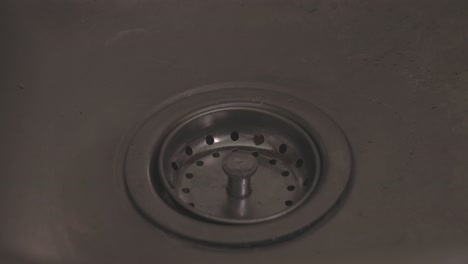 close-up shot of water flowing down a kitchen sink as hands wash dishes