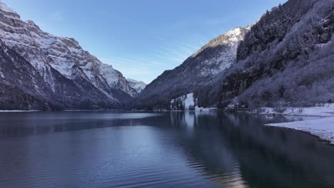 Klöntalersee lake in Glarus, Switzerland, nestled in Swiss alps, serene destination pristine waters, drone pushes forwards of majestic snowy mountains and breathtaking natural beauty during winter.