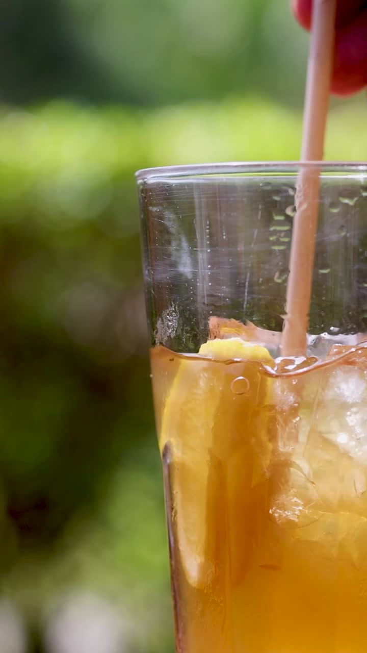 Mano che mescola un cocktail arancione in un ambiente esterno soleggiato