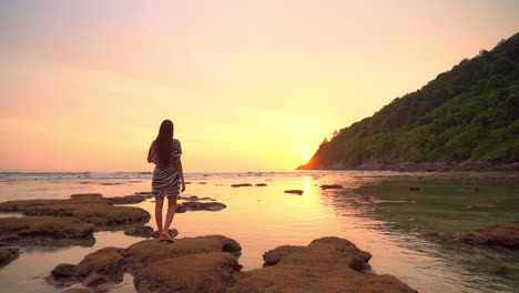girl enjoying beautiful golden sunset on secluded rocky beach