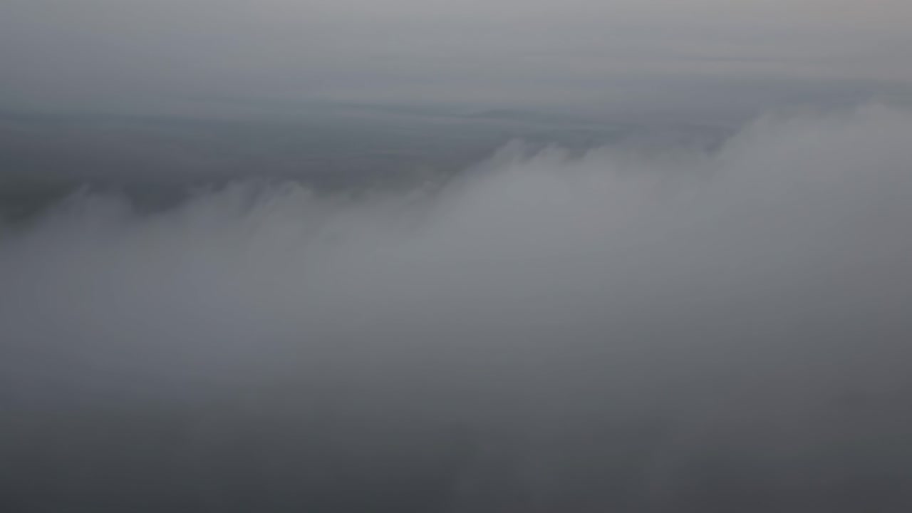 Dense fog blanketing misty landscape, generating ethereal mood during early morning hours, gray sky obscuring distant terrain with low visibility, perfect for atmospheric nature backgrounds