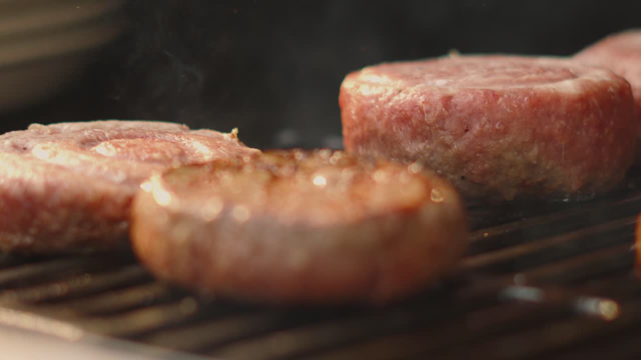 Focus Pull from Flipping Foreground Raw Beef Burger to Background Patties in Natural Summer Evening Sunlight. Cooking Meat on the BBQ Grill