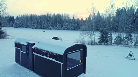 trailer and sauna by a frozen lake and frosty forest in the countryside - aerial flyover