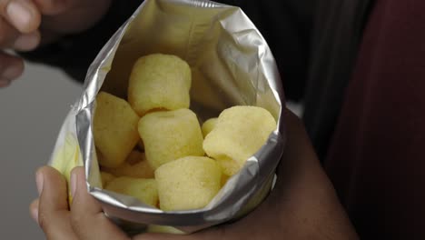 cerca de un joven comiendo anillos de maíz crujientes bocadillos salados en una bolsa de papel. comida rápida o comida chatarra bocadillos concepto no saludable.