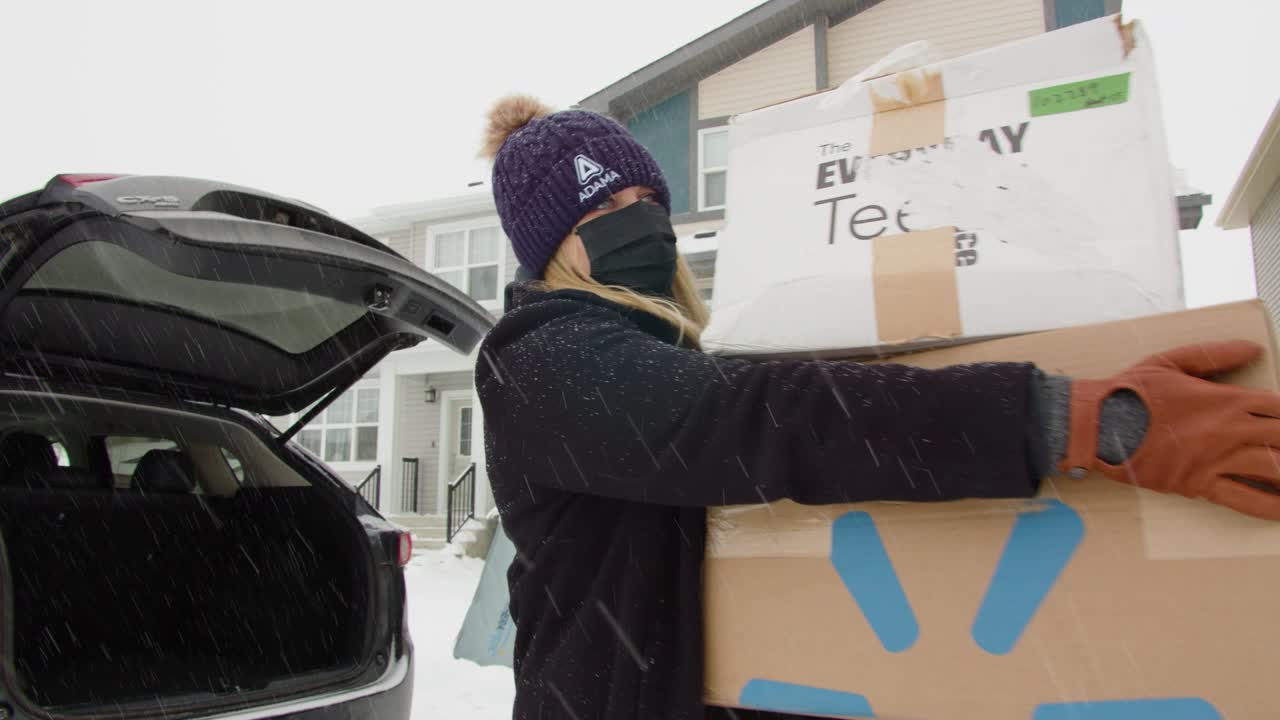 Two women unloading boxes and a mattress from a car in the snow