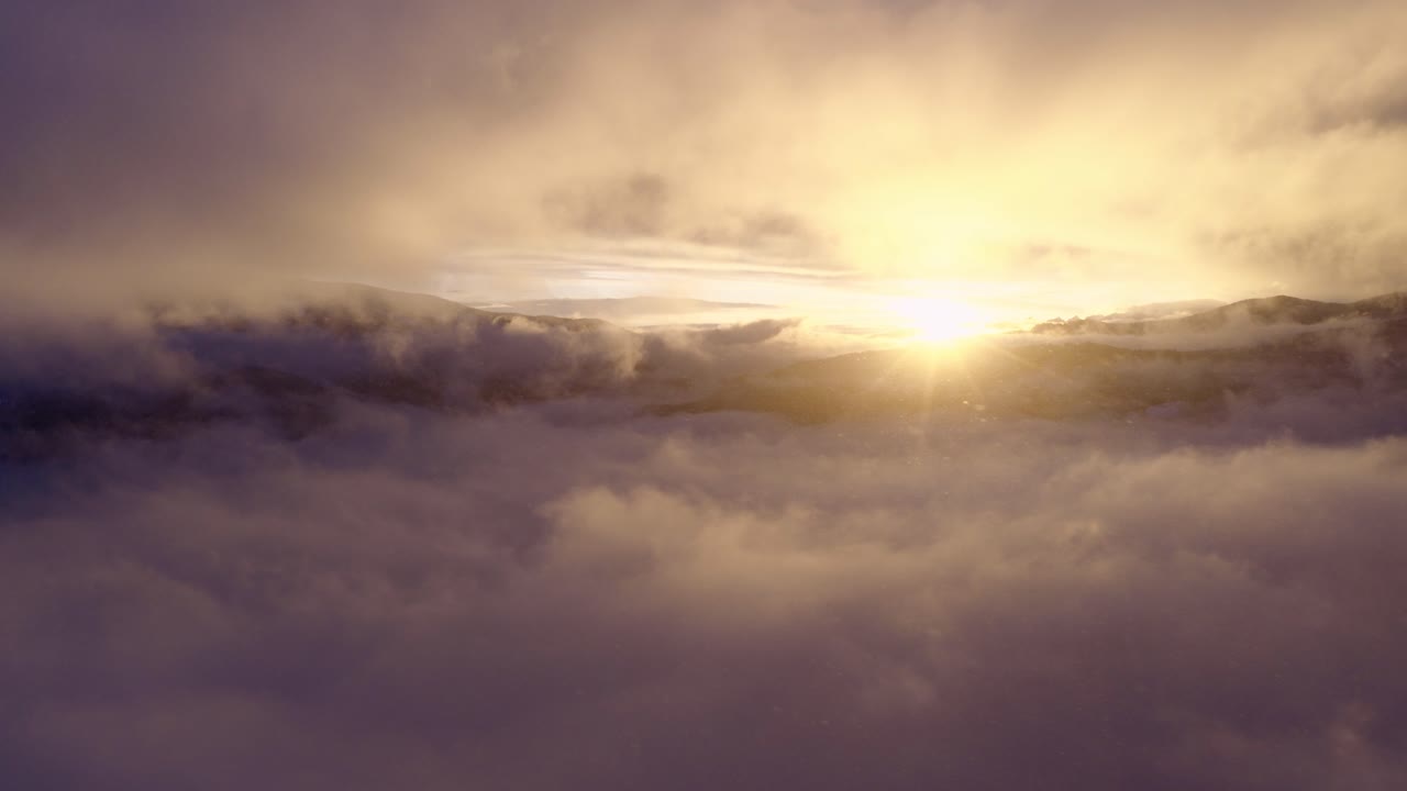 Val di Fiemme, Trentino, Italia - La luce dorata del sole sorge sopra un mare di nuvole, illuminando dolcemente l'orizzonte montano - Ripresa aerea con drone.