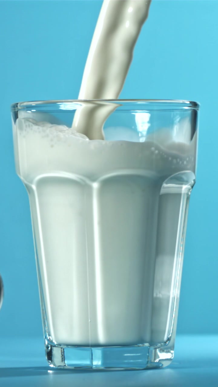 Mleko w zwolnionym tempie wlewane do szklanki na niebieskim tle