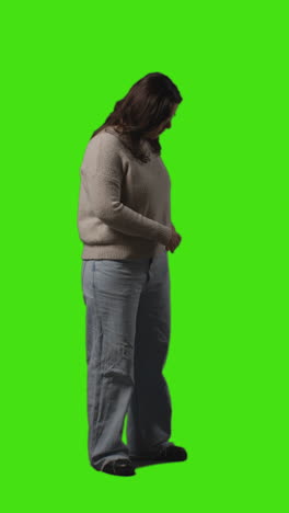 Vertical-Video-Full-Length-Shot-Of-Young-Woman-Answering-Call-On-Mobile-Phone-Standing-Against-Green-Screen-1